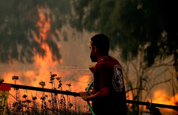 A man uses a garden hose to water down dry vegetation as the Alisal fire burns at the edges of a ranch near Goleta, California, on Oct. 12.