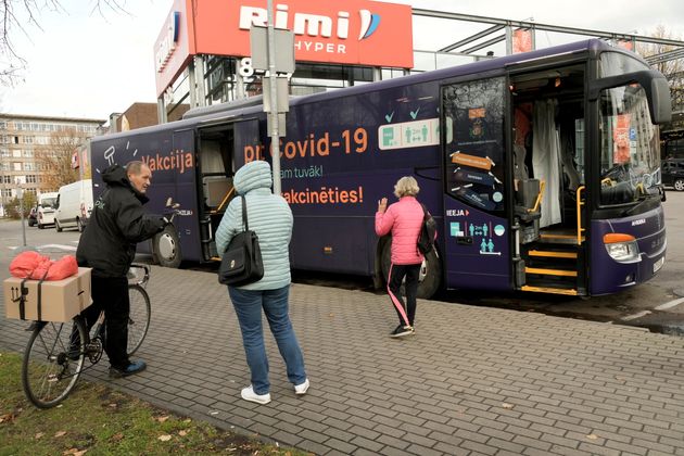 Kόσμος περιμένει να μπει μέσα σε ένα κινητό λεωφορείο εμβολιασμού για την ασθένεια του κορωνοϊού (COVID-19) δίπλα στο εμπορικό κέντρο στη Ρίγα της Λετονίας, 19 Οκτωβρίου 2021. Οι πινακίδες σε ένα λεωφορείο γράφουν 