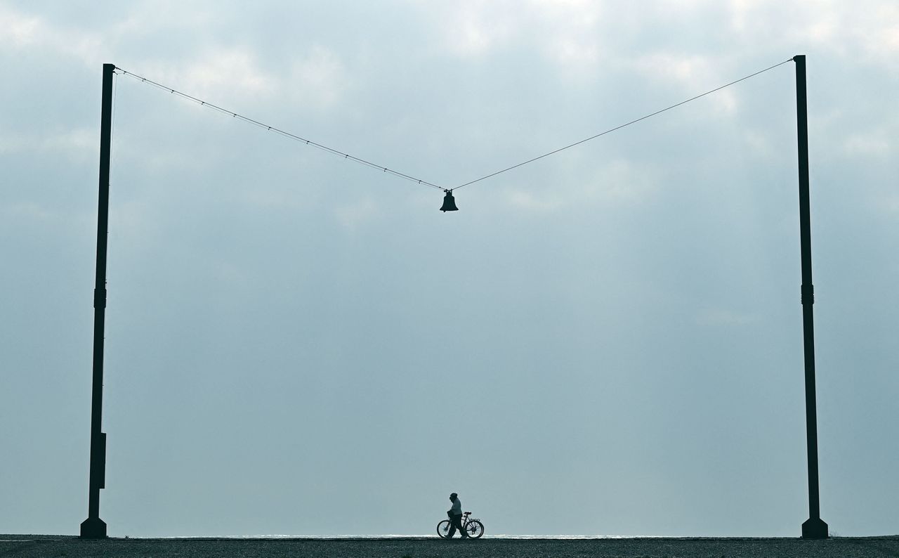 A man pushes a bicycle past an art installation titled "Out of Tune" featuring a 16th-century tenor bell from Scraptoft Church in Leicestershire, by Norwegian artist A K Dolven, on the beachfront in Folkestone, England, on Oct. 19.