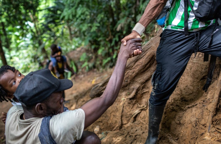 A Colombian guide helps a Haitian father and daughter up a steep mountain slope near Colombia's border with Panama on Oct. 20, 2021. The 66-mile trek through dense rainforest and mountains is considered the most difficult stretch for migrants traveling from South America to the United States.