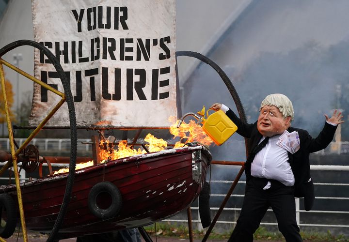 Performers from Ocean Rebellion dressed as U.K. Prime Minister Boris Johnson set light to the sail of a small boat which reads "Your Children's Future" as they burn stacks of money on the banks of the River Clyde in Glasgow, Scotland, close to the site of the upcoming U.N. COP26 climate conference.