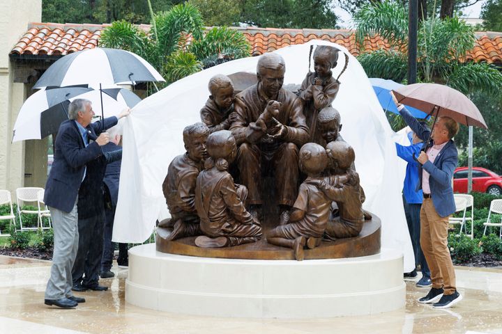 In this photo provided by Rollins College, school officials unveil a sculpture honoring alumnus and beloved children's TV host Mister Rogers, Thursday, Oct. 28, 2021, on campus in Winter Park, Fla. (Scott Cook/Rollins College via AP)