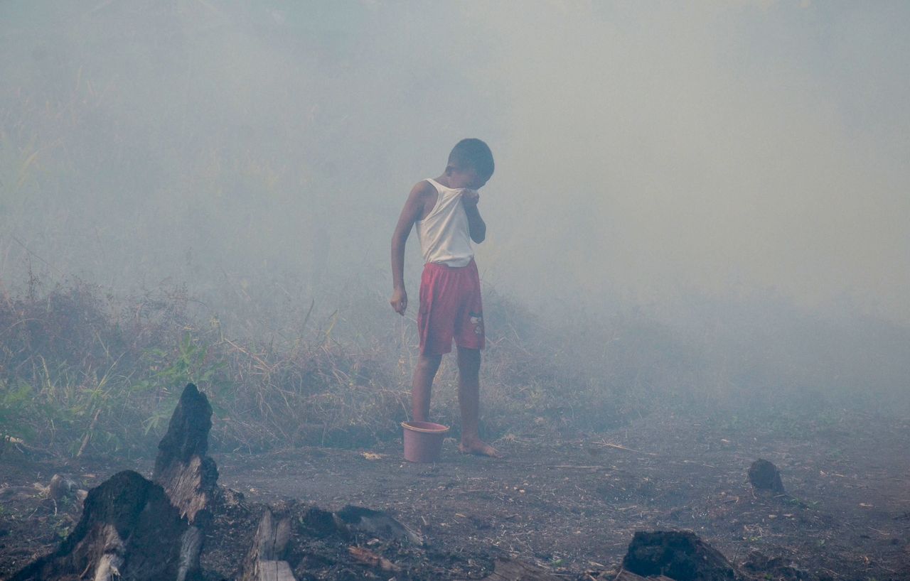 A young boy covers his eyes as smoke shrouds his neighborhood in Indonesia. 