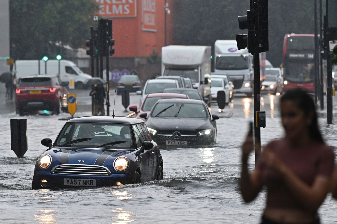 Cars drive through deep water on a flooded road in London in July 2021 during heavy rain.