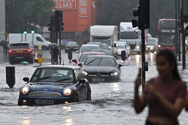 Cars drive through deep water on a flooded road in London in July 2021 during heavy