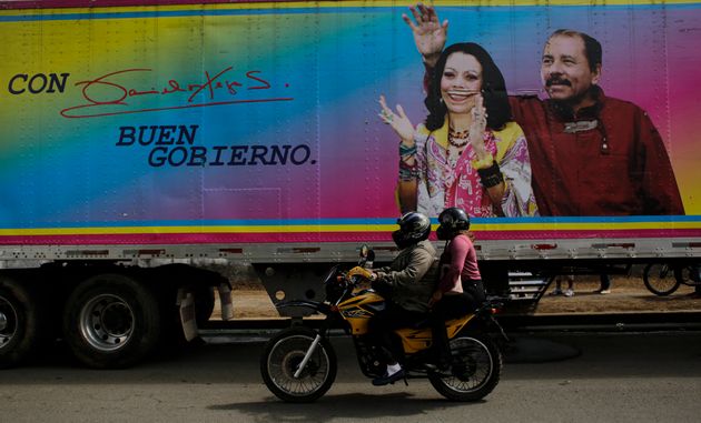 Motocicleta pasando por delante de un cartel electoral en un camión de Daniel Ortega, presidente...