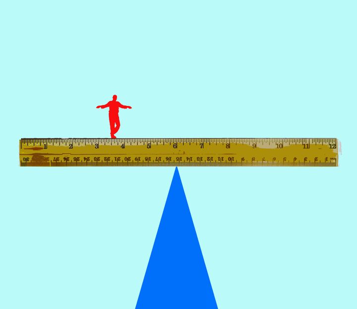 man balancing on a ruler on a triangle