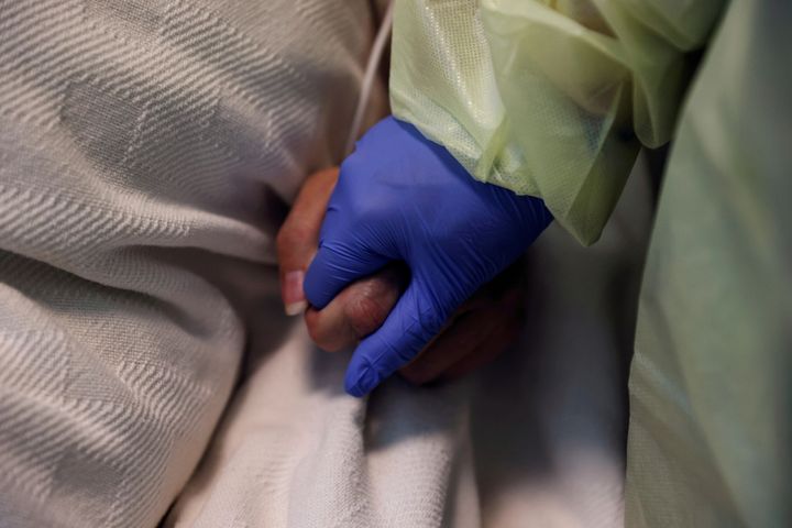 Μια γυναίκα με τον εξοπλισμό ατομικής προστασίας της (PPE) κρατά το χέρι ενός ασθενούς θετικού στον κορονοϊό.