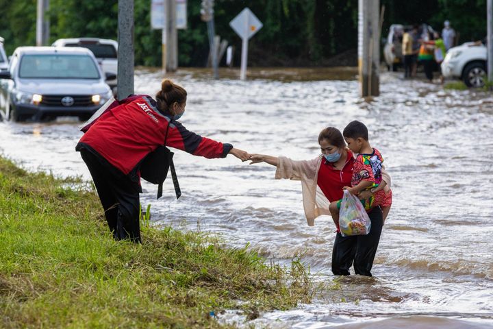A woman and her child are seen getting help to cross the road after a heavy rainfall in Thailand after a flash flood