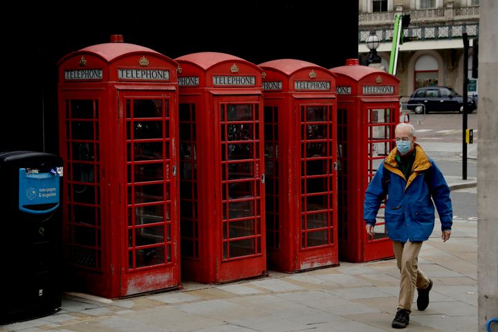 Ένας άνδρας που φοράει μάσκα περνά μπροστά από τους κόκκινους τηλεφωνικούς θαλάμους στο Λονδίνο