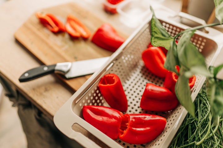 Chef slices sweet orange bell pepper on the background of vegetable ingredients, on a black background. Cooking salad. Healthy and wholesome food, cuisine and cooking, recipe book.