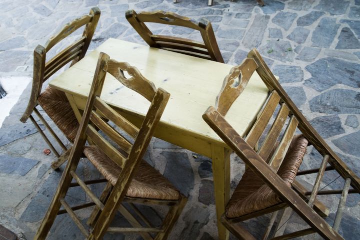 The detail from the village Leptopoda on island Chios, Greece. Four greek old and used traditional chairs leaned to the table, on the stony ground. Greek taverna style.
