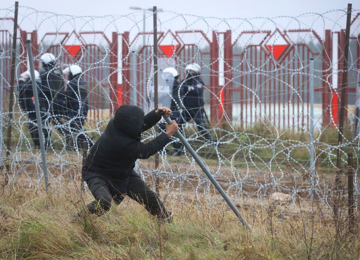Άνδρας επιχειρεί να γκρεμίσει μέρος του φράχτη από συρματόπλευμα στα σύνορα Πολωνίας Λευκορωσίας, υπό το βλέμμα αστυνομικών.<br> (Leonid Shcheglov/BelTA via AP)