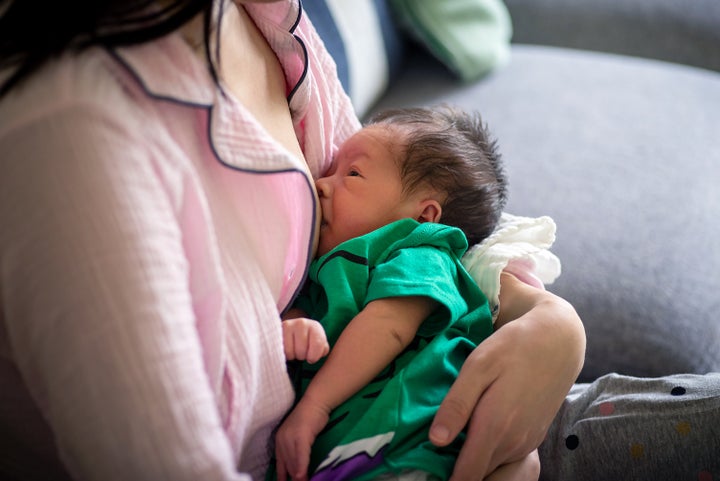 Woman holding and breastfeeding 10 days old newborn baby boy on her lap sitting on the sofa in the living room at home