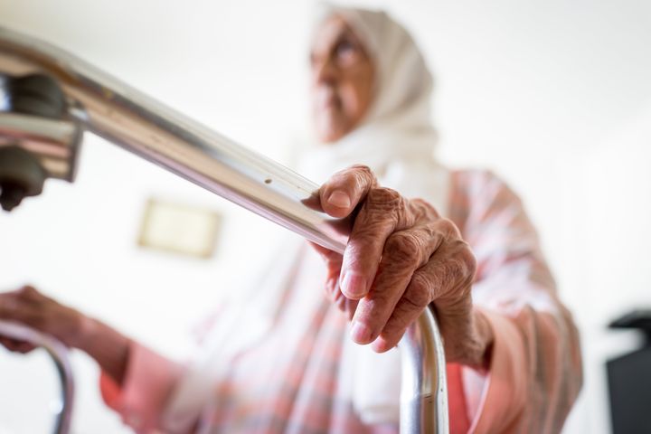 Very old Middle Eastern woman using walker with closeup on hands