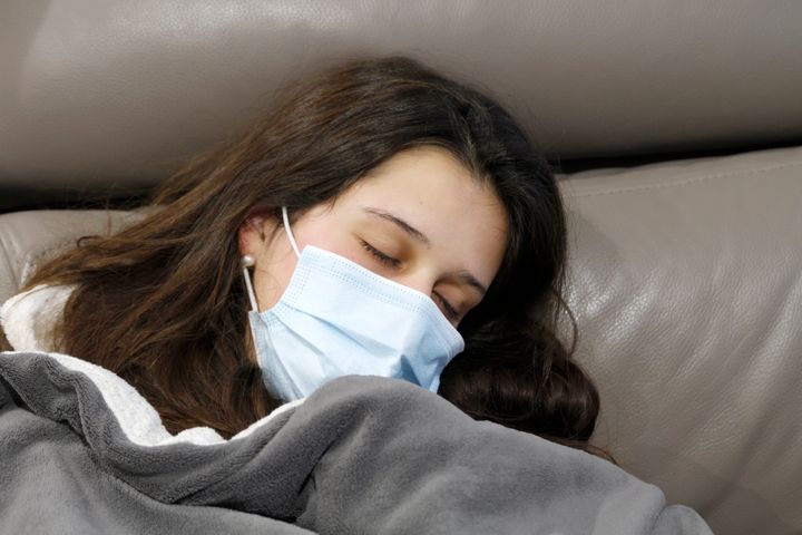 Sick woman with protective face mask sleeping on sofa