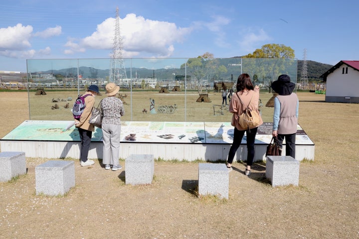 「安満遺跡」を紹介するガラスサイン。手前のブロックに腰掛けると、目の前に弥生時代の暮らしが広がる。