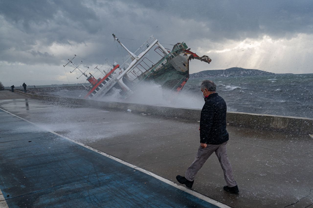 A man walks near a boat that has capsized due to strong winds in Istanbul, on Tuesday. Four people were killed and dozens injured as the city was hit by high winds on Monday.