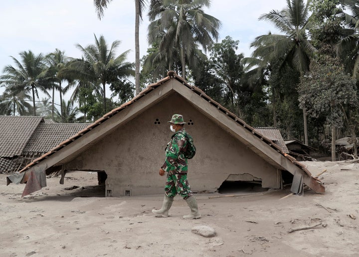 An Indonesian soldier walks by a house buried in the ash following the eruption of Mount Semeru in Lumajang district, East Java province, Indonesia, Sunday, Dec. 5, 2021. The death toll from eruption of the highest volcano on Indonesia's most densely populated island of Java has risen with scores still missing, officials said Sunday as rain continued to pound the region and hamper the search.(AP Photo/Trisnadi)