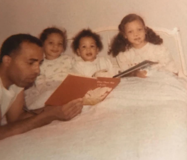 La autora (extremo derecho) y sus hermanas, Karina (izquierda) y Suzette, escuchando a su padre leer un cuento antes de dormir en 1969.