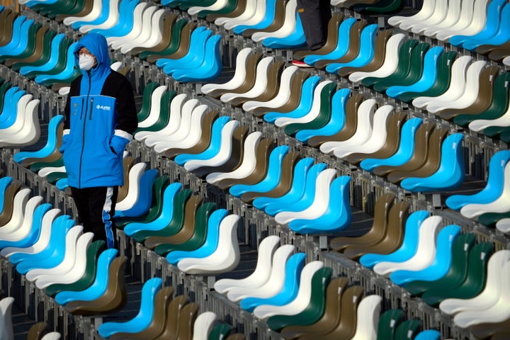 A staff member wearing a face mask to protect against COVID-19 stands amid empty spectator seats at the FIS Snowboard Cross World Cup, a test event for the 2022 Winter Olympics, at the Genting Resort Secret Garden in Zhangjiakou in northern China's Hebei Province, Sunday, Nov. 28, 2021. (AP Photo/Mark Schiefelbein)