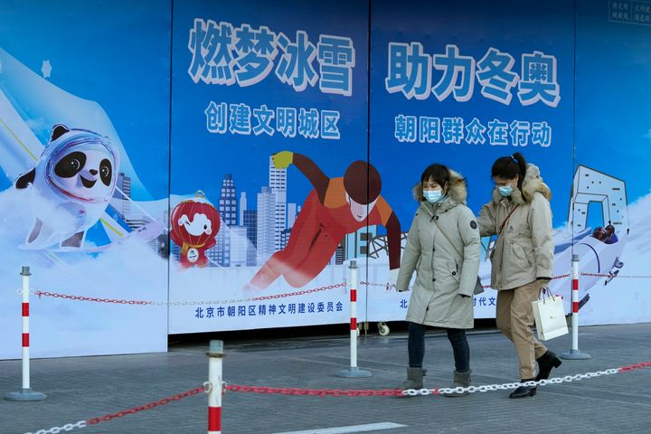 Residents wearing masks pass by propaganda boards promoting the upcoming Beijing Winter Olympics in Beijing, China, Monday, Nov. 22, 2021. Beijing reiterates its commitment to hosting a frugal and green Winter Olympics ahead of the February sporting event, promising to make the games "simple and excellent." (AP Photo/Ng Han Guan)