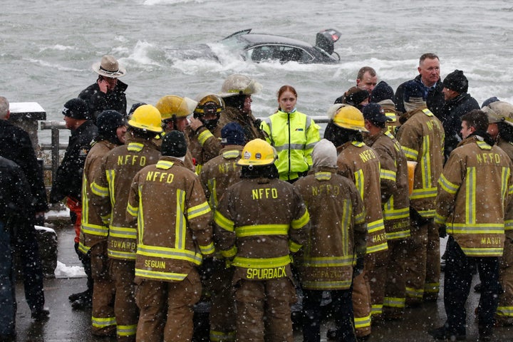 Emergency personnel gather at the edge of the river where a woman was removed from a submerged vehicle.