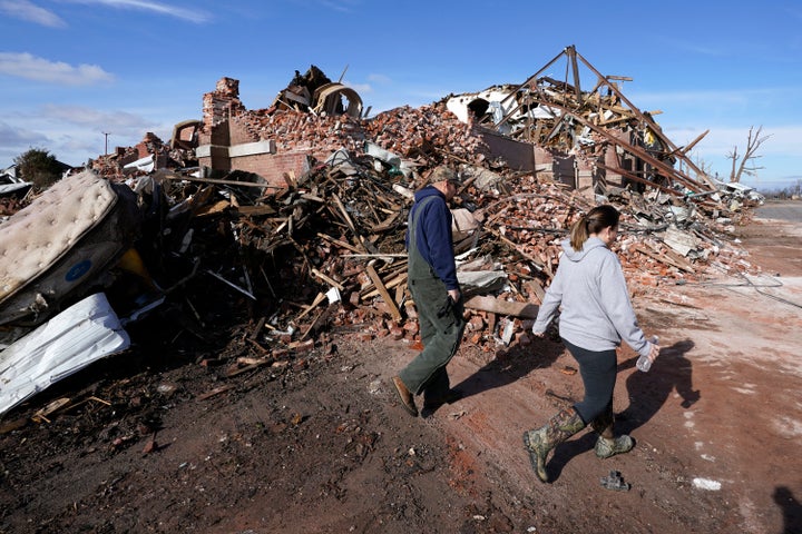 People walk past a destroyed building Saturday, Dec. 11, 2021, in Mayfield, Ky. (AP Photo/Mark Humphrey)
