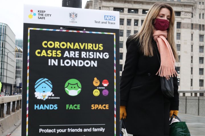 A woman walking past a coronavirus information sign on London Bridge.