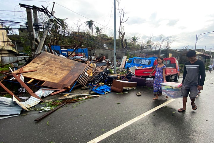 Residents carry what's left of their belongings as they walk past damaged homes due to Typhoon Rai in Surigao city.