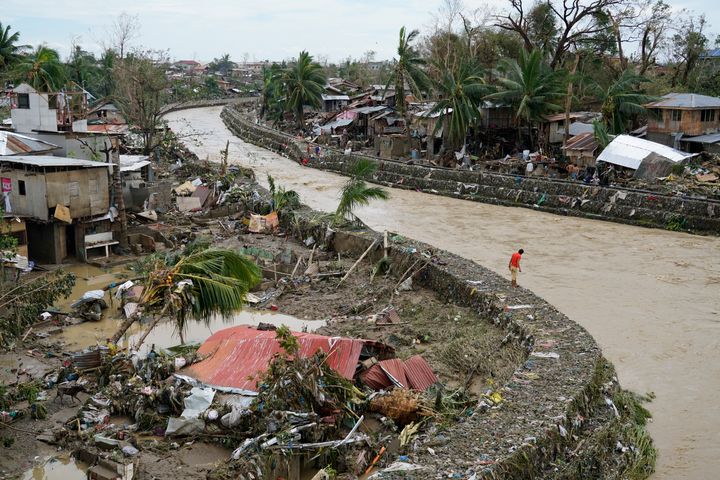 A man stands beside damaged homes along a swollen river due to Typhoon Rai in Talisay, Cebu province.