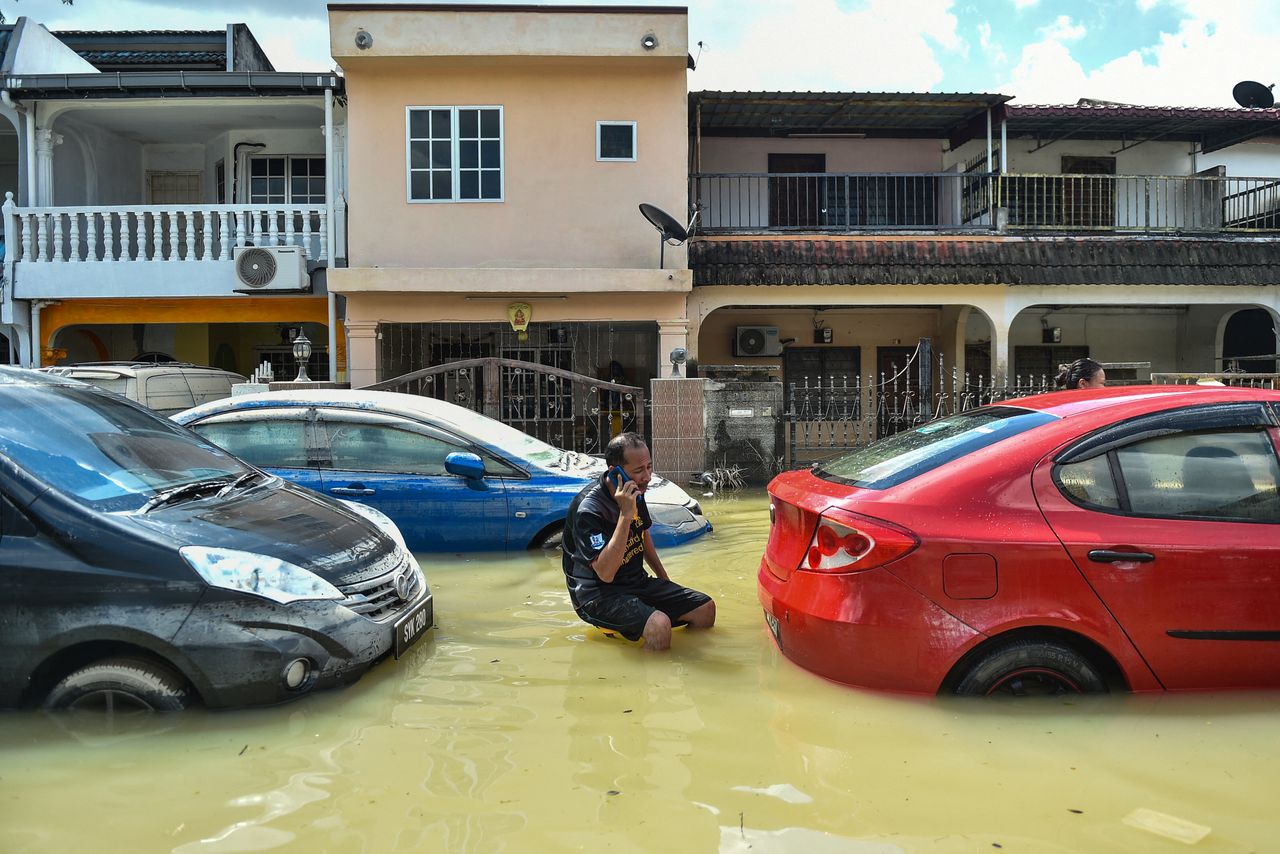 A man uses a mobile phone as he sits between cars amid floodwaters in Shah Alam, Selangor, on Tuesday, as Malaysia faces massive floods that have left at least 14 dead and more than 70,000 displaced.