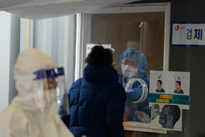 A medial worker in a booth takes a nasal sample from a man at a makeshift testing site in Seoul, South Korea, Monday, Dec. 27, 2021. (AP Photo/Ahn Young-joon)