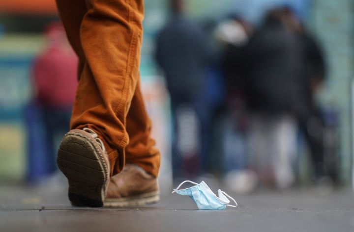 A man walks past a disgarded face mask on the ground, outside a shopping centre in downtown Mainz, Germany, Monday, Dec. 27, 2021. (Frank Rumpenhorst/dpa via AP)