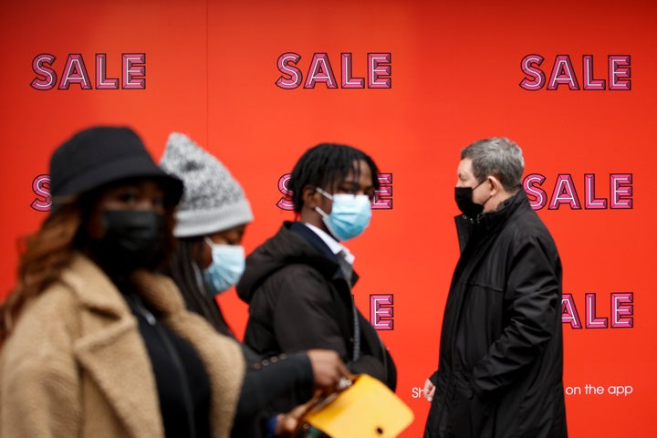 Shoppers wearing face masks to guard against COVID-19 walk past a sale poster covering a window of department store Selfridges on Oxford Street in London, Monday, Dec. 27, 2021. (AP Photo/David Cliff)