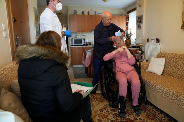 O νοσοκόμος Παναγιώτης Μποζιονέλος (αριστερά) ετοιμάζεται να χορηγήσει την τρίτη ενισχυτική δόση εμβολίου Pfizer-BioNTech για τον COVID-19, στην Μαρία Γεωργιοπούλου, καθώς ο σύζυγός της φοράει την μάσκα στο πρόσωπό του. 22  2021. Public health authorities in Greece have stepped up a campaign to deliver booster shots to seniors and people with mobility difficulties at home – with one agency outside Athens hiring taxis to take healthcare workers to where the vaccinations are needed. (AP Photo/Thanassis Stavrakis)