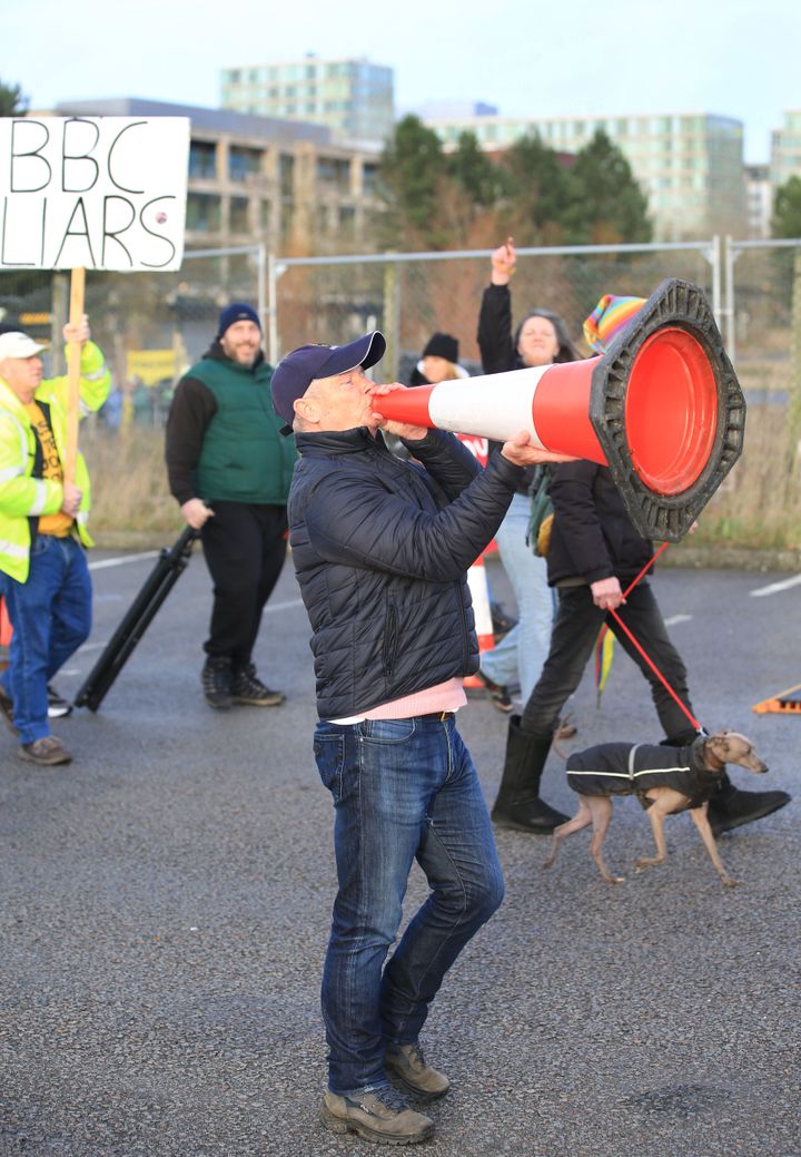 A protester uses a traffic cone as a megaphone as demonstrators disrupt the vaccination centre.