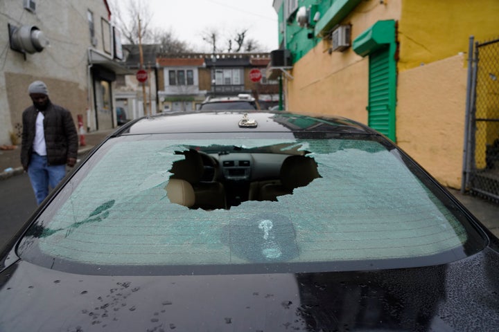 A man walks past a parked vehicle with a bullet holes in the rear window on Friday, Dec. 31, 2021, in Philadelphia. Two gunmen fired more than 65 rounds on a Philadelphia street last night, sending nighttime pedestrians on a busy block teeming with markets and restaurants scrambling for cover and injuring six people, at least one of them critically, police said Friday. (AP Photo/Michael Perez)