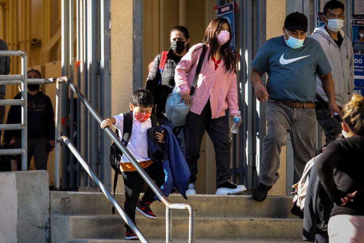 Masked adults and children leave through the front gates at John G. Whittier School, as school returns after winter break and a spike in positive COVID-19 cases in Long Beach, Calif., on Jan. 3, 2022.