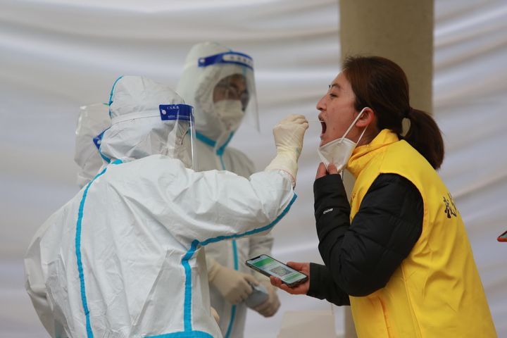 A medical worker takes a throat swab sample on a woman during the 11th round of the all-inclusive Covid-19 test on the residents in Qujiang district in Xi'an in Shaanxi province on Jan. 4, 2022. 