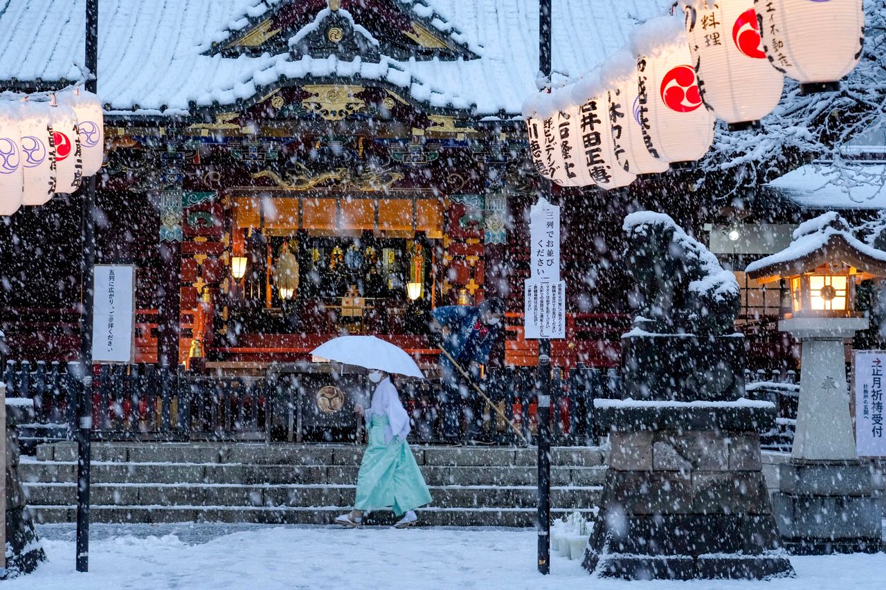 A shrine maiden walks past the main shrine while a worker clears the steps as snow falls down Thursday in Tokyo.