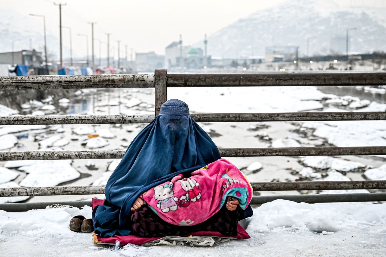 A burqa-clad Afghan woman sits with a child on her lap as she seeks alms from passersby on a bridge covered with snow in Kabul on Thursday.