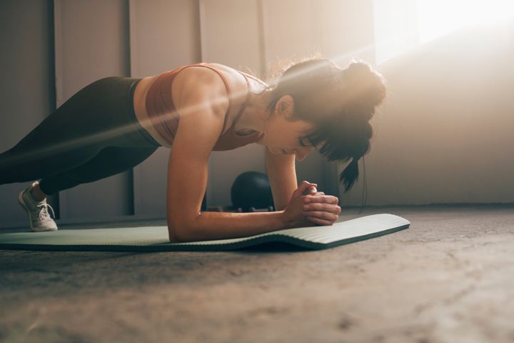 Serious woman in sportswear doing plank exercise on a exercise mat at home.