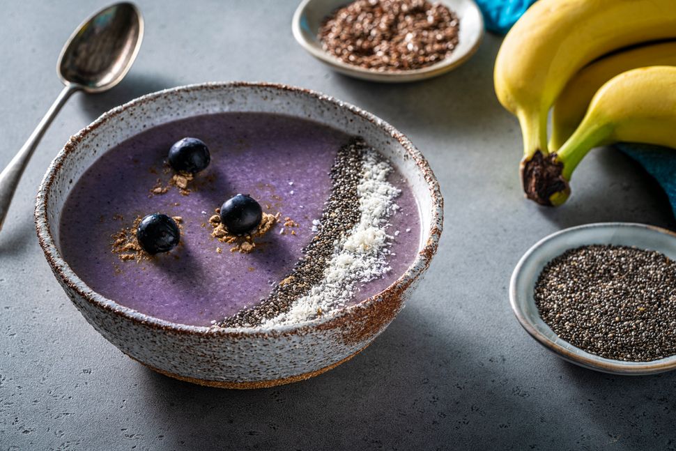 Blueberry smoothie breakfast bowl vegan recipe including ingredients as blueberries, banana, walnuts, oat flakes, maca powder, chia seeds and almond milk.