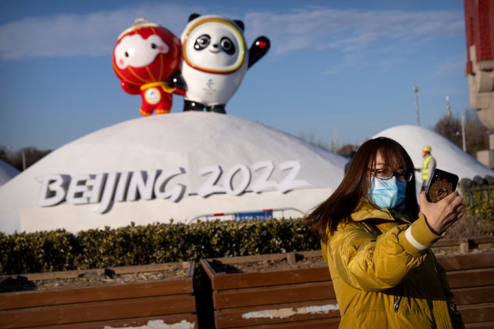 A woman wearing a face mask to protect against coronavirus poses for a selfie with a display of the Winter Paralympic mascot Shuey Rhon Rhon, left, and Winter Olympic mascot Bing Dwen Dwen near the Olympic Green in Beijing, on Jan. 12, 2022.