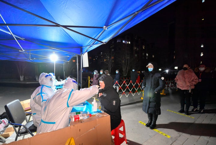 In this photo released by China's Xinhua News Agency, a worker wearing a protective suit swabs for a coronavirus test at a COVID-19 testing site in northern China's Tianjin Municipality, on Jan. 12, 2022.