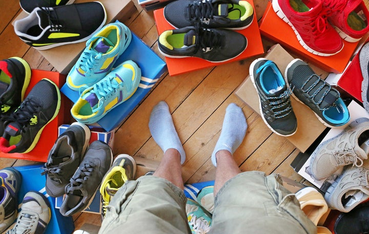 Man deciding what to wear surrounded by various trainers and casual footwear.