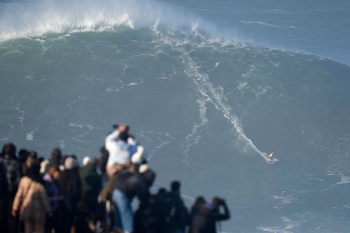 Θεατές παρακολουθούν με κομμένη την ανάσα καθώς ένα θεόρατο κύμα καταδιώκει έναν από τους πρωταθλητές του σερφ στην Praia do Norte της Πορτογαλίας. Ναζαρέ 8 Ιανουαρίου 2022. (AP Photo/Armando Franca)