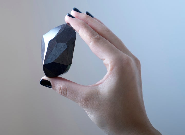 An employee of Sotheby's Dubai presents a 555.55 Carat Black Diamond "The Enigma" to be auctioned at Sotheby's Dubai gallery, in Dubai, United Arab Emirates, Monday, Jan. 17, 2022. (AP Photo/Kamran Jebreili)