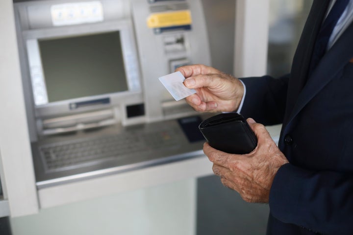 Un anciano saca su tarjeta para usarla en un cajero automático.